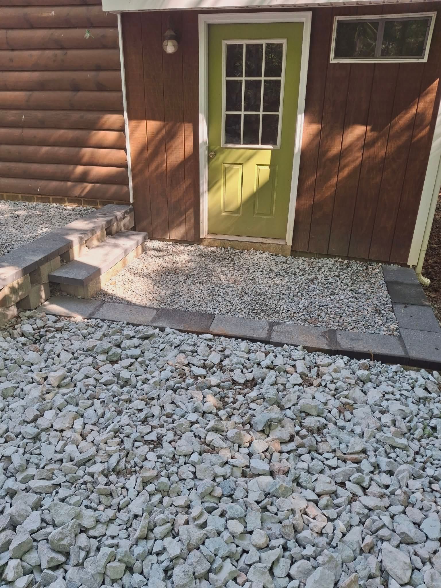 Green door on a wooden cabin, with gravel path and steps outside.