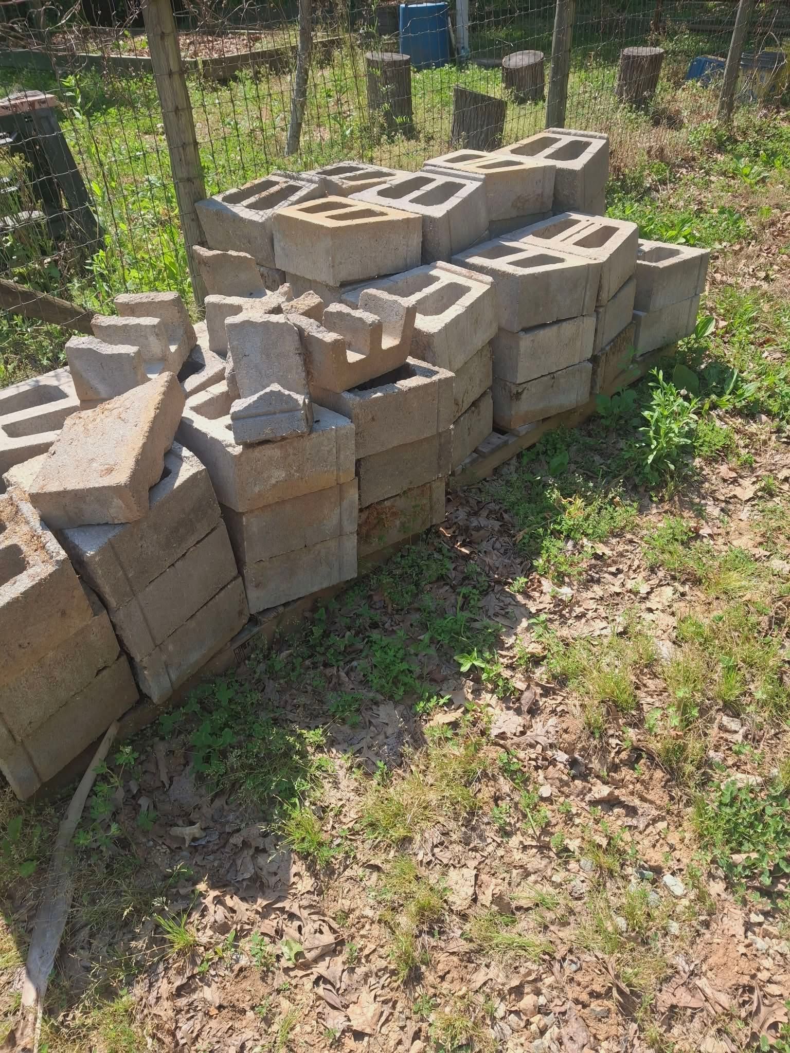 Stacked tan cinder blocks forming a low wall in a grassy outdoor area with trees in the background