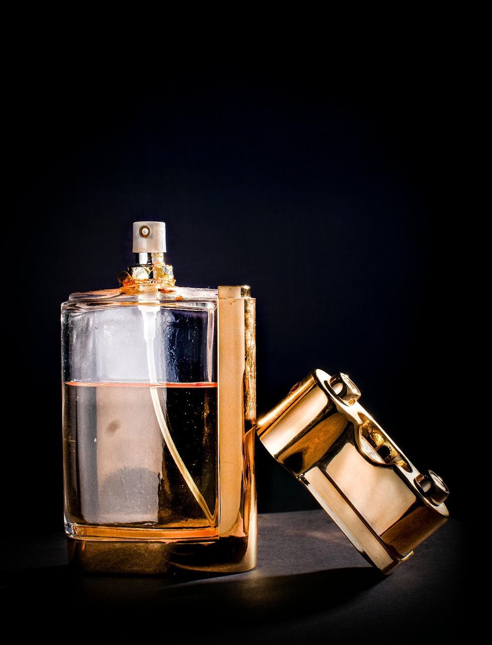Parfumflesje met gouden rand en loszittende dop tegen een donkere achtergrond; amberkleurige vloeistof zichtbaar.