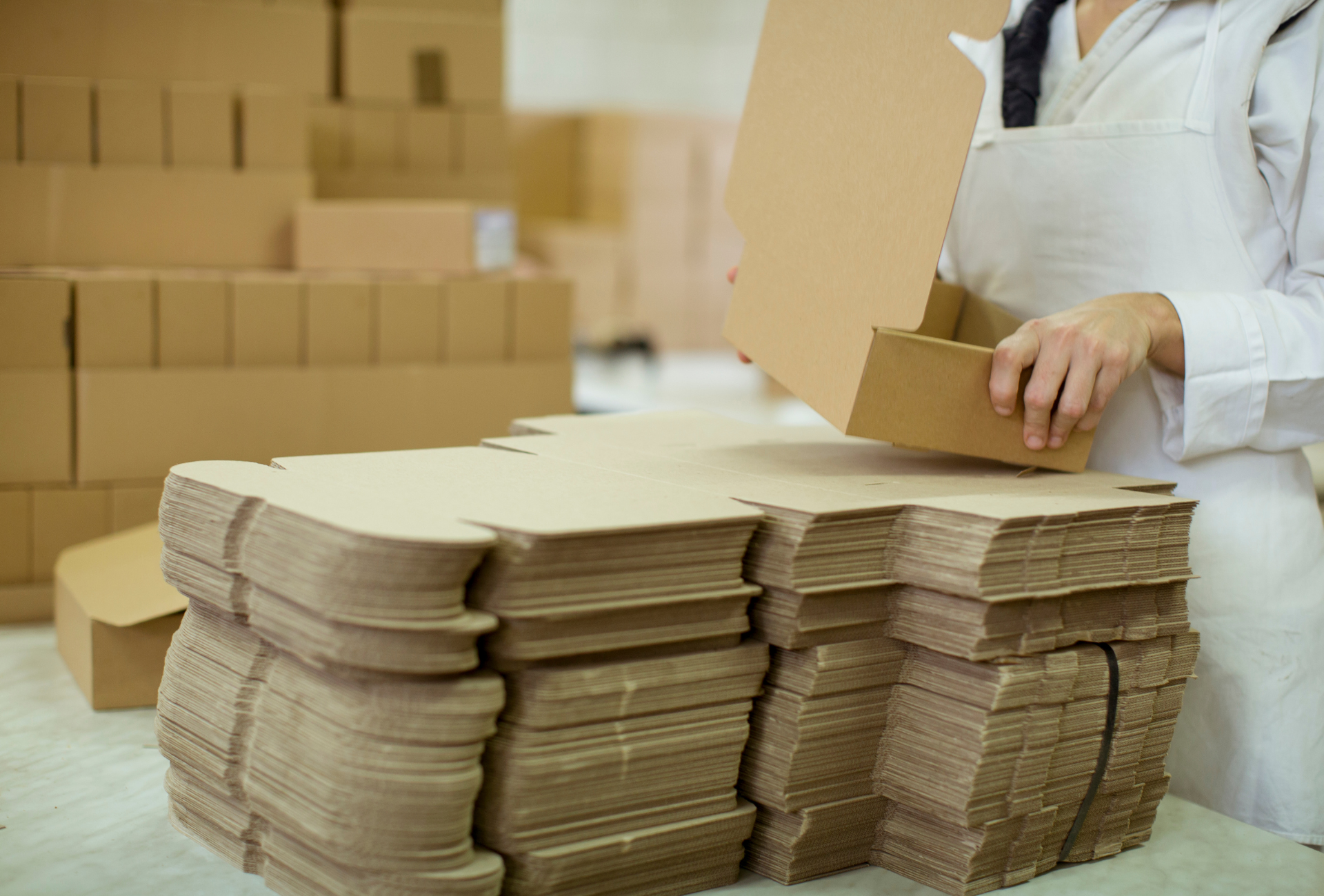 A person is holding a cardboard box in front of a pile of cardboard boxes.