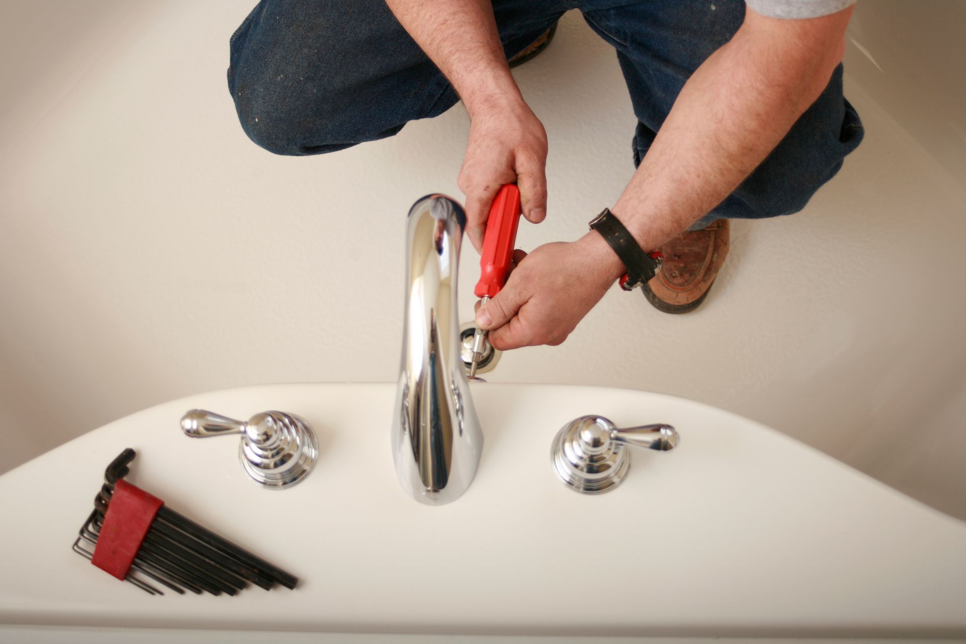 Person using pliers to work on a faucet in a white bathtub.