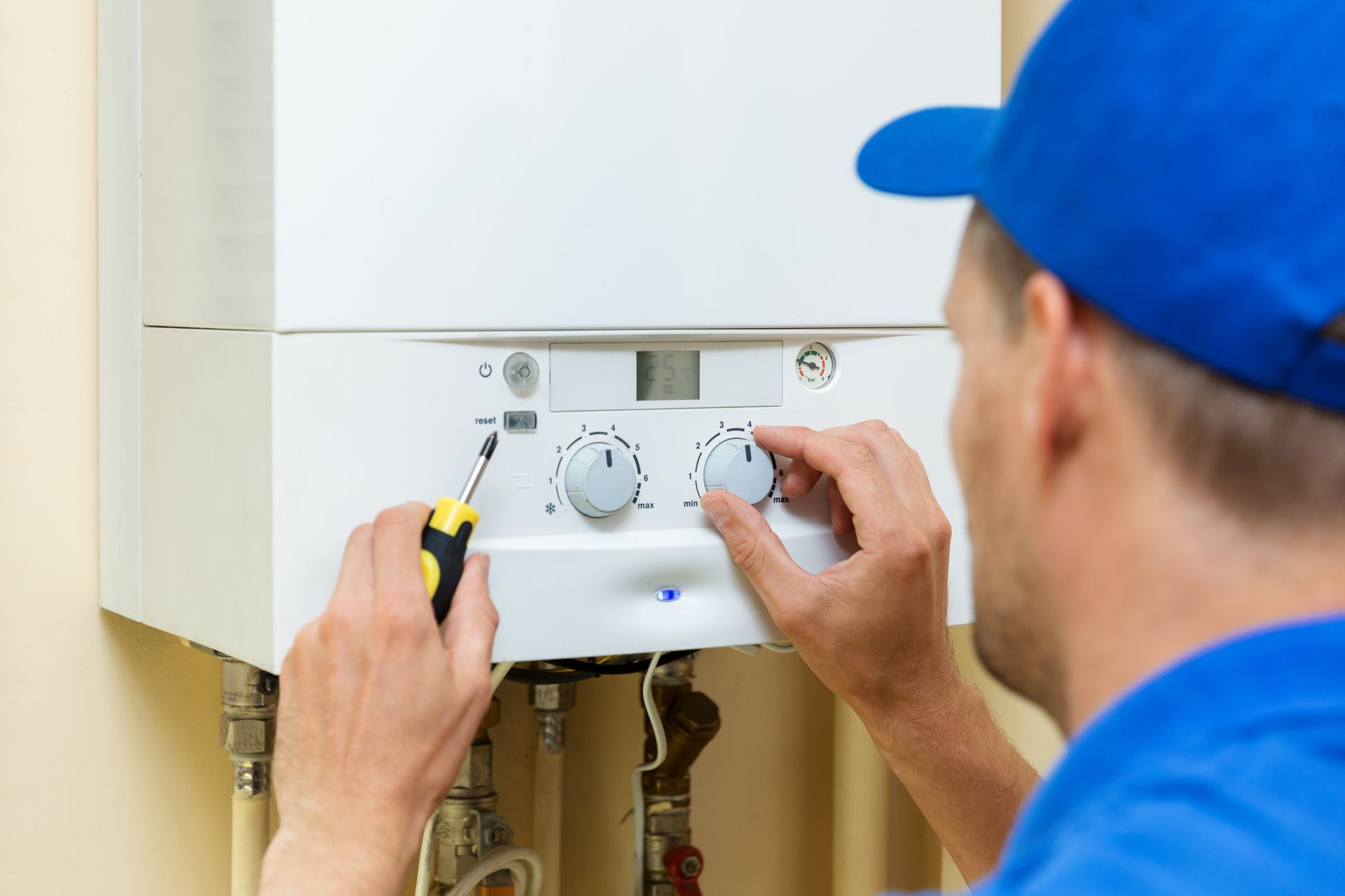 Plumber in blue adjusting controls on a white boiler with a screwdriver.