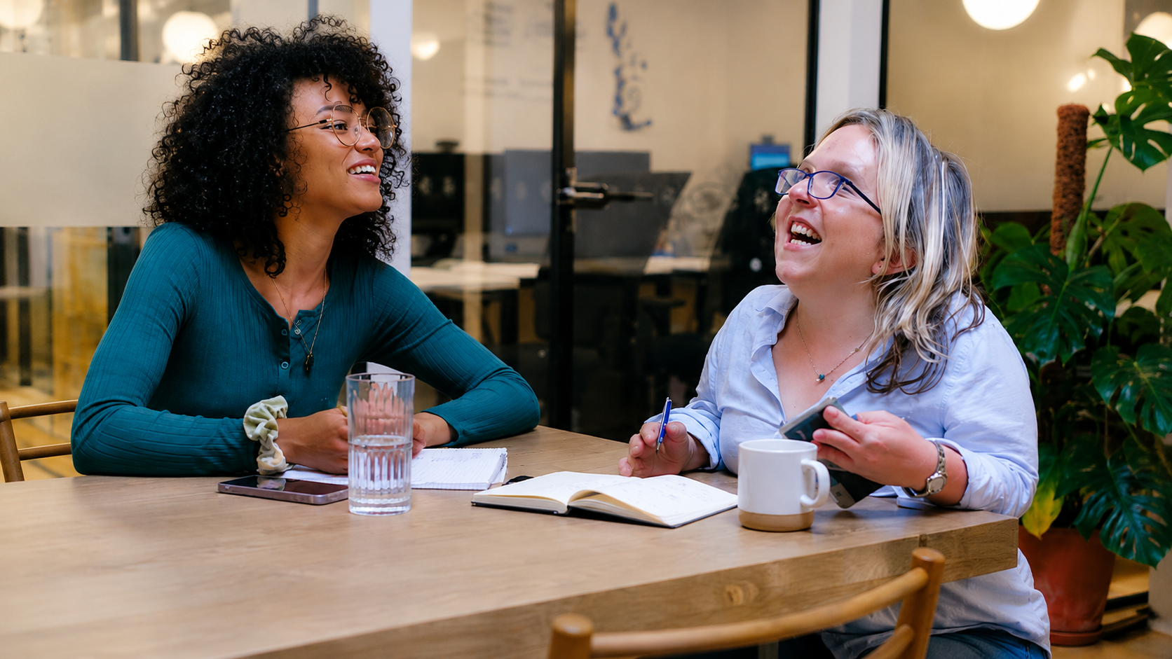 NDIS Participant and mental health worker smiling and talking at a café table with drinks and an open notebook