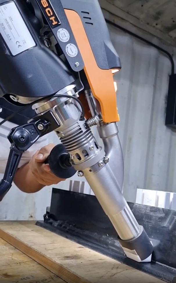 Un trabajador utiliza una herramienta eléctrica naranja para cortar metal en un taller industrial.
