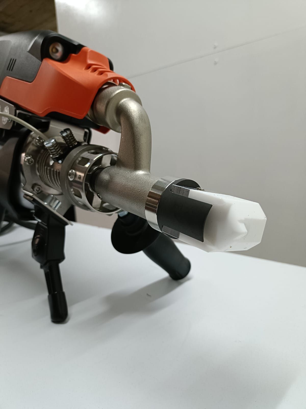 Primer plano de una herramienta eléctrica naranja y plateada con una boquilla blanca sobre una superficie blanca.
