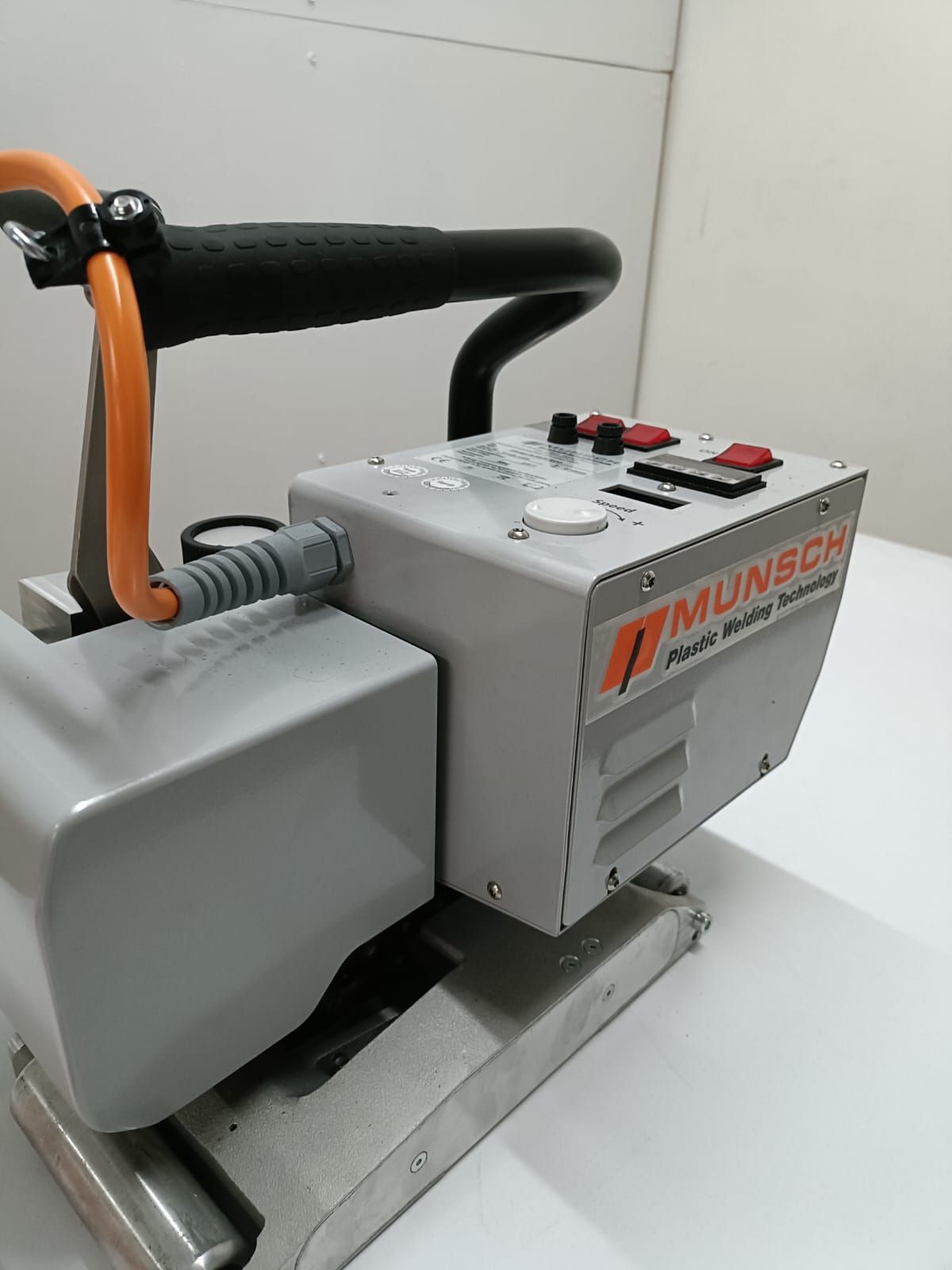 Máquina industrial portátil de color naranja y negro con asa y botones de control sobre una base metálica.