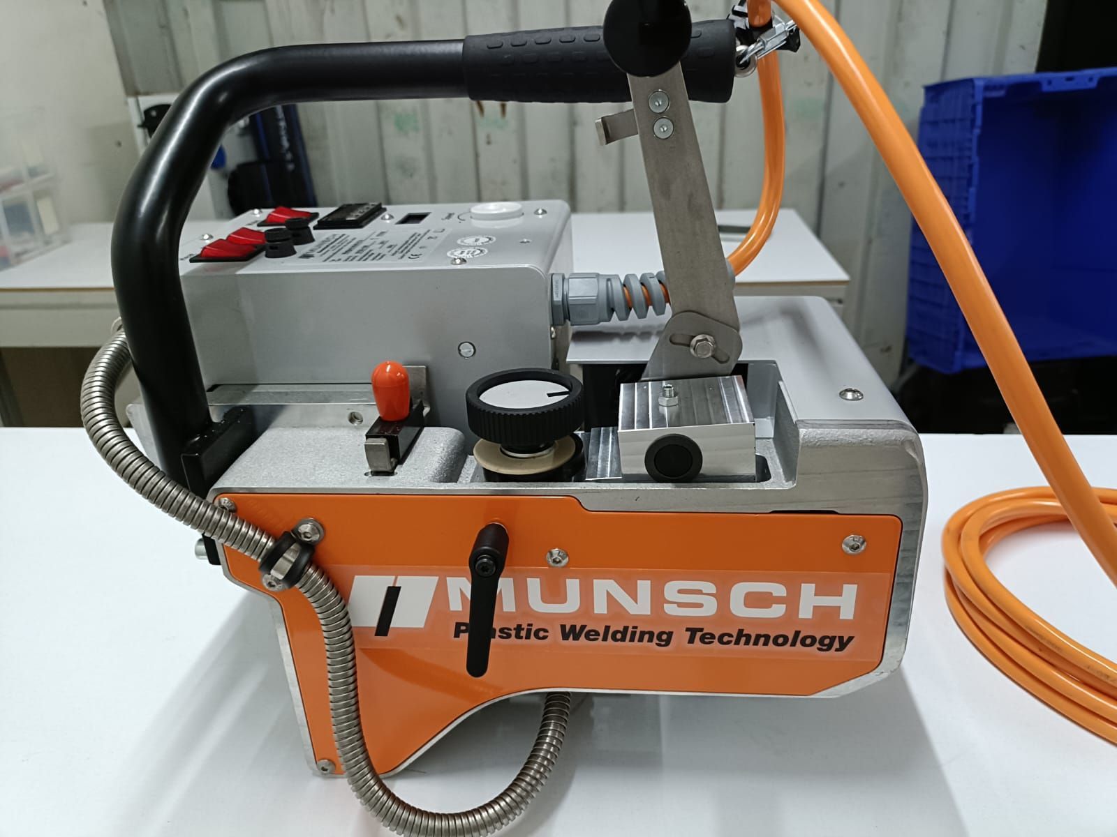 Máquina portátil HUNSCH de color naranja y plateado con mangueras y manómetro en el suelo de un taller.