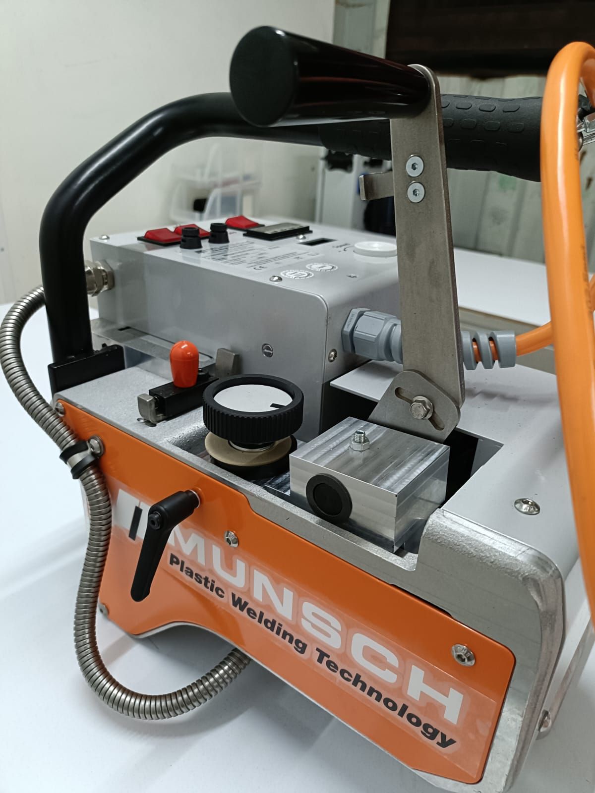 Máquina portátil de metal con etiqueta naranja “MUSC”, asa negra e interruptores de control.