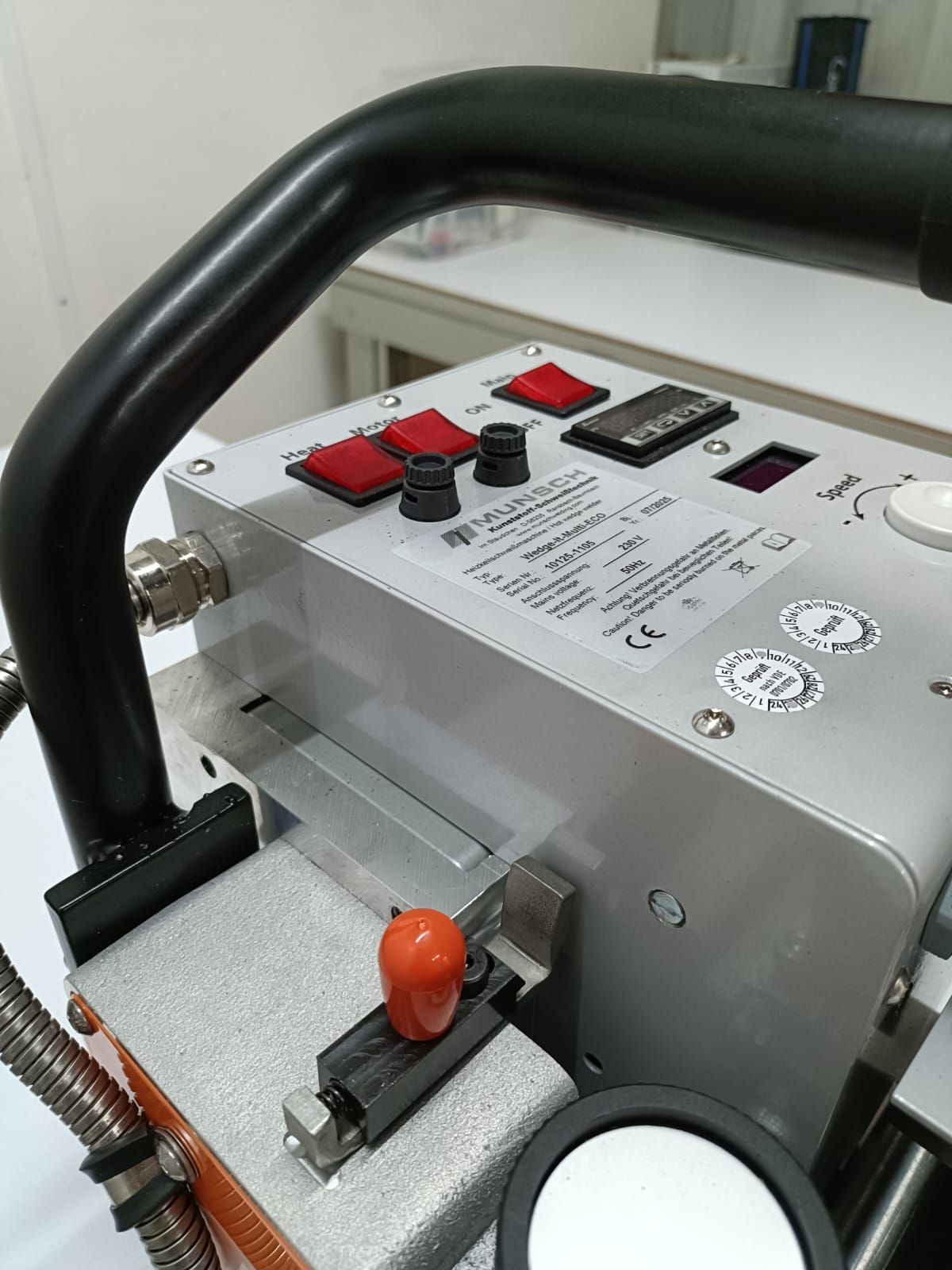 Primer plano de un panel de control con interruptores rojos y negros y una palanca naranja en una máquina de metal.