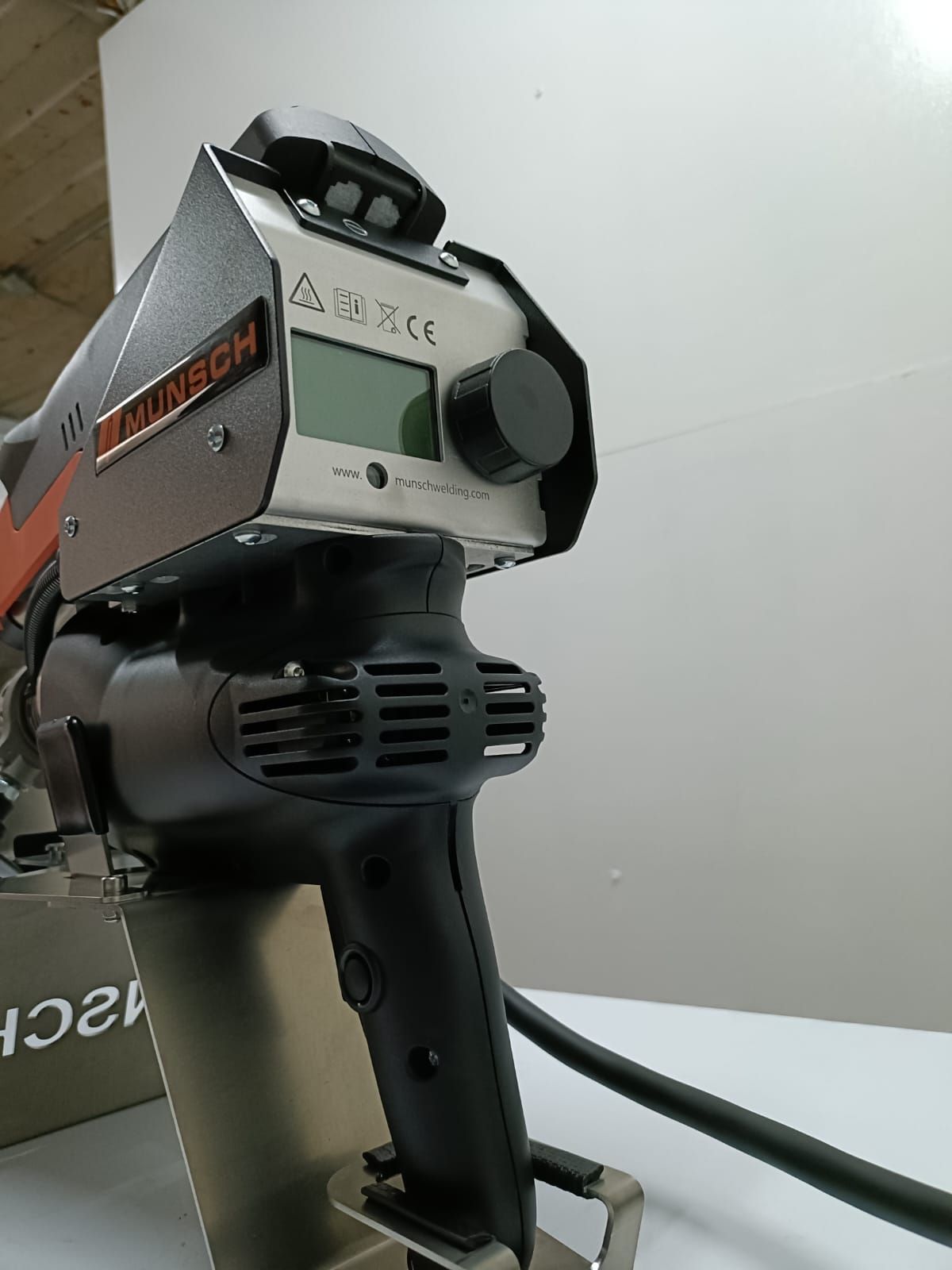 Herramienta eléctrica industrial con mango negro y carcasa gris, mostrada en primer plano contra una pared lisa.
