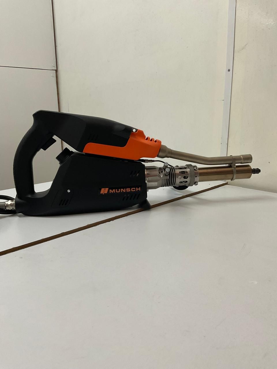 Herramienta eléctrica de mano negra y naranja sobre un suelo blanco contra una pared.