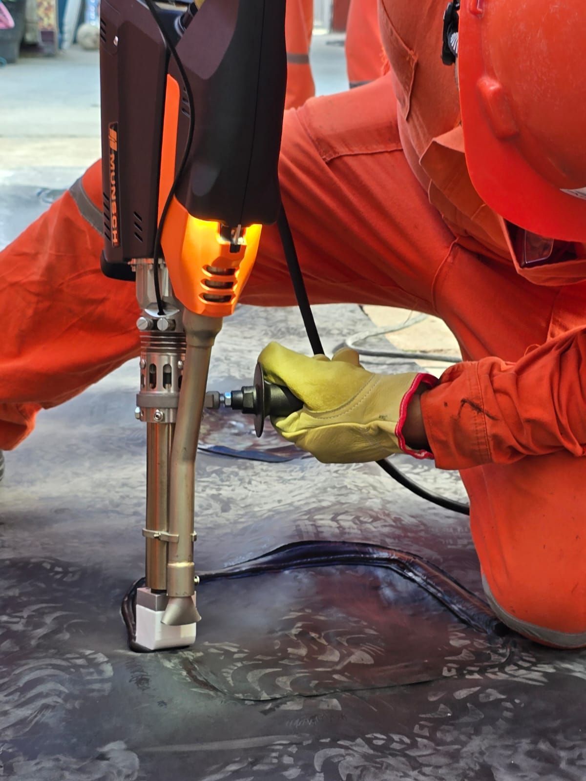 Trabajador con equipo de protección naranja utilizando una herramienta caliente sobre una superficie metálica.