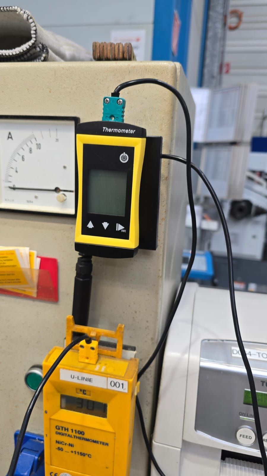Dispositivo de control industrial amarillo montado en un equipo de laboratorio, con cables conectados y un medidor cerca.