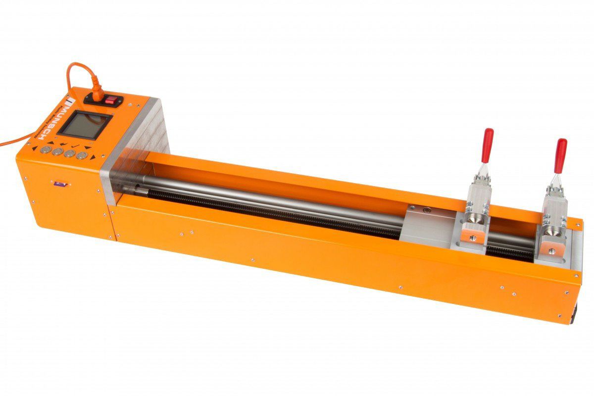 Máquina industrial naranja con dos abrazaderas en un largo riel metálico, aislada sobre fondo blanco.