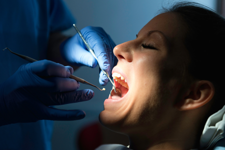 Dentist examining open mouth with dental tools and bright overhead light