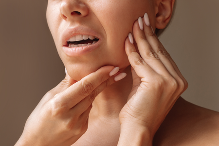 Close-up of a person touching their jaw and cheek, showing mouth pain or discomfort.