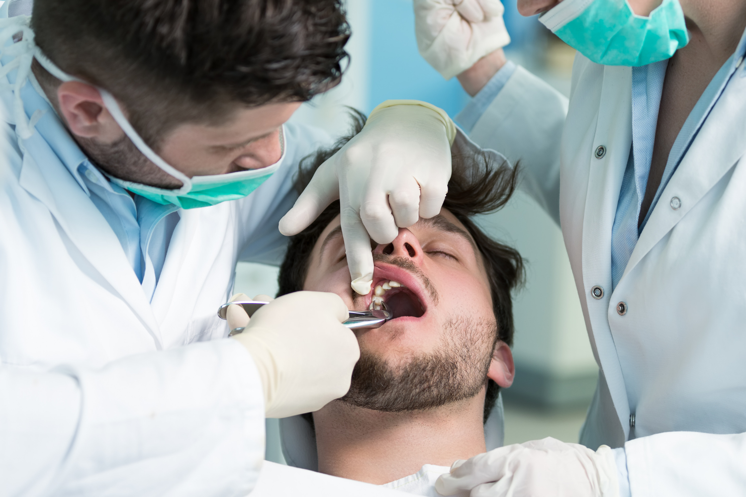 Dentist examining a patient’s open mouth while two assistants stand nearby in a clinic