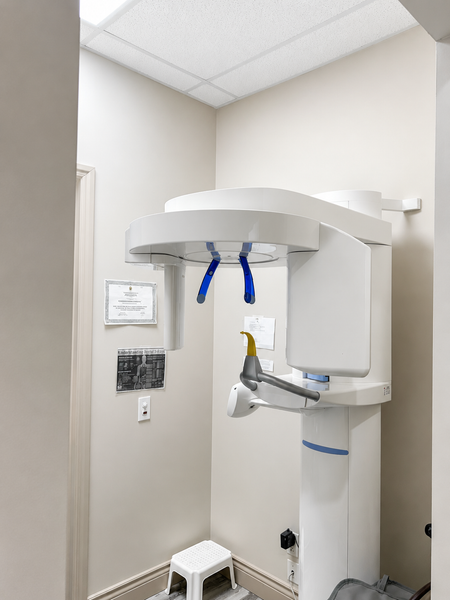 Dental X-ray machine in a small exam room with beige walls and a ceiling-mounted unit
