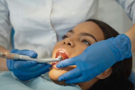 Dentist using a handheld tool on a patient’s open mouth, with blue gloves and clinical setting