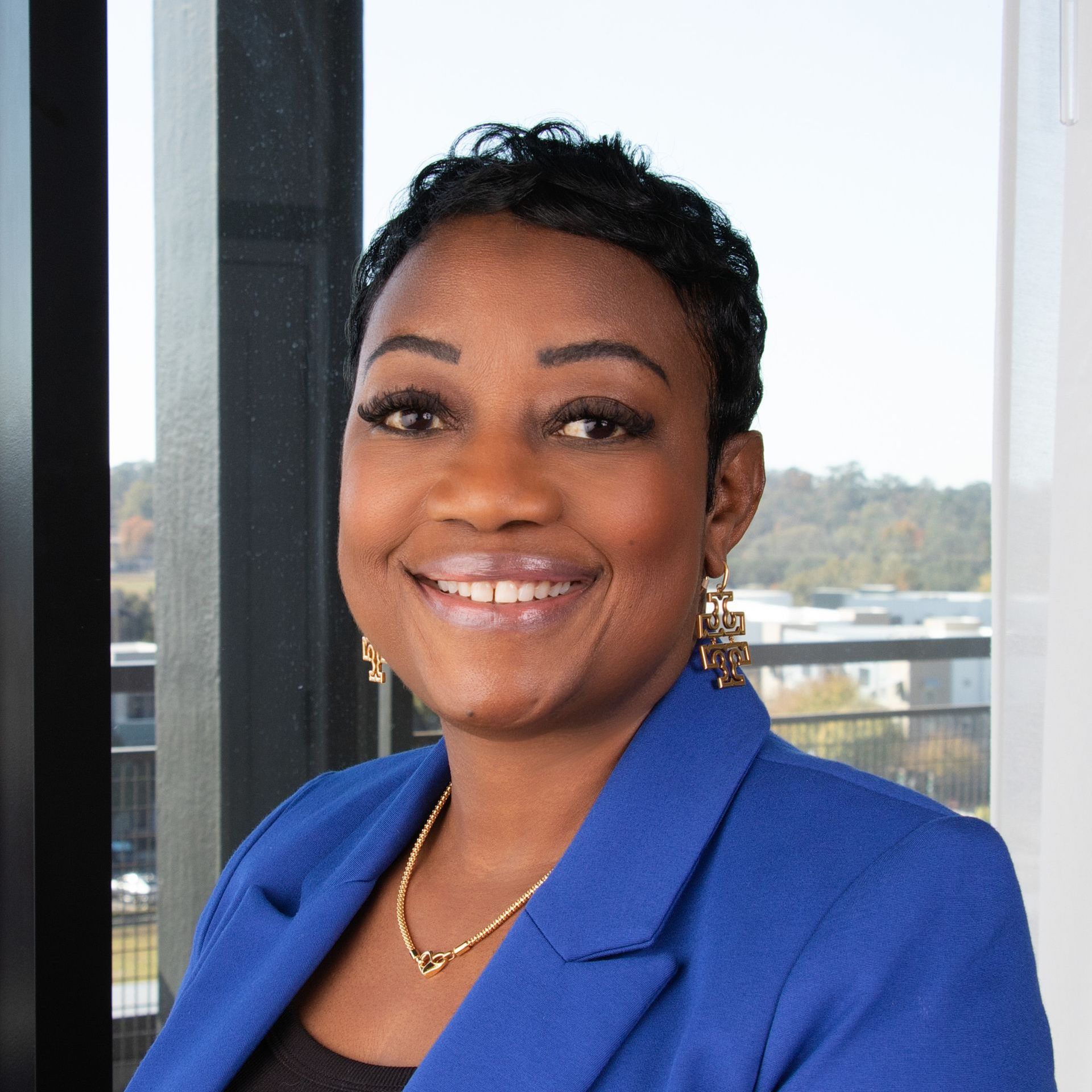 A woman wearing a blue jacket and earrings is smiling for the camera.