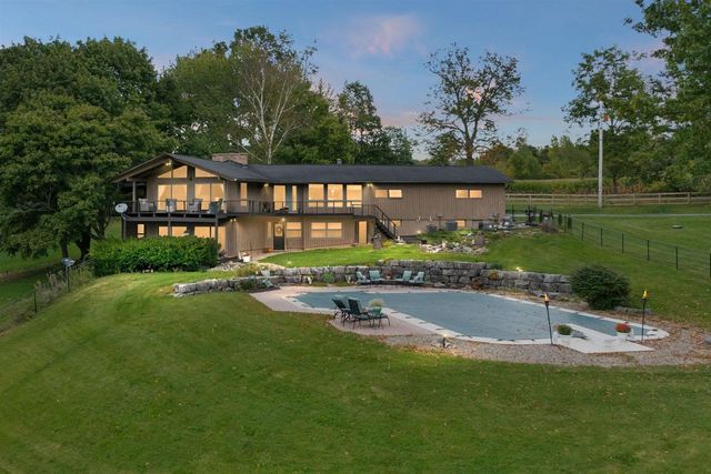 Large single-family home with expansive backyard, patio area, and outdoor seating surrounded by trees.