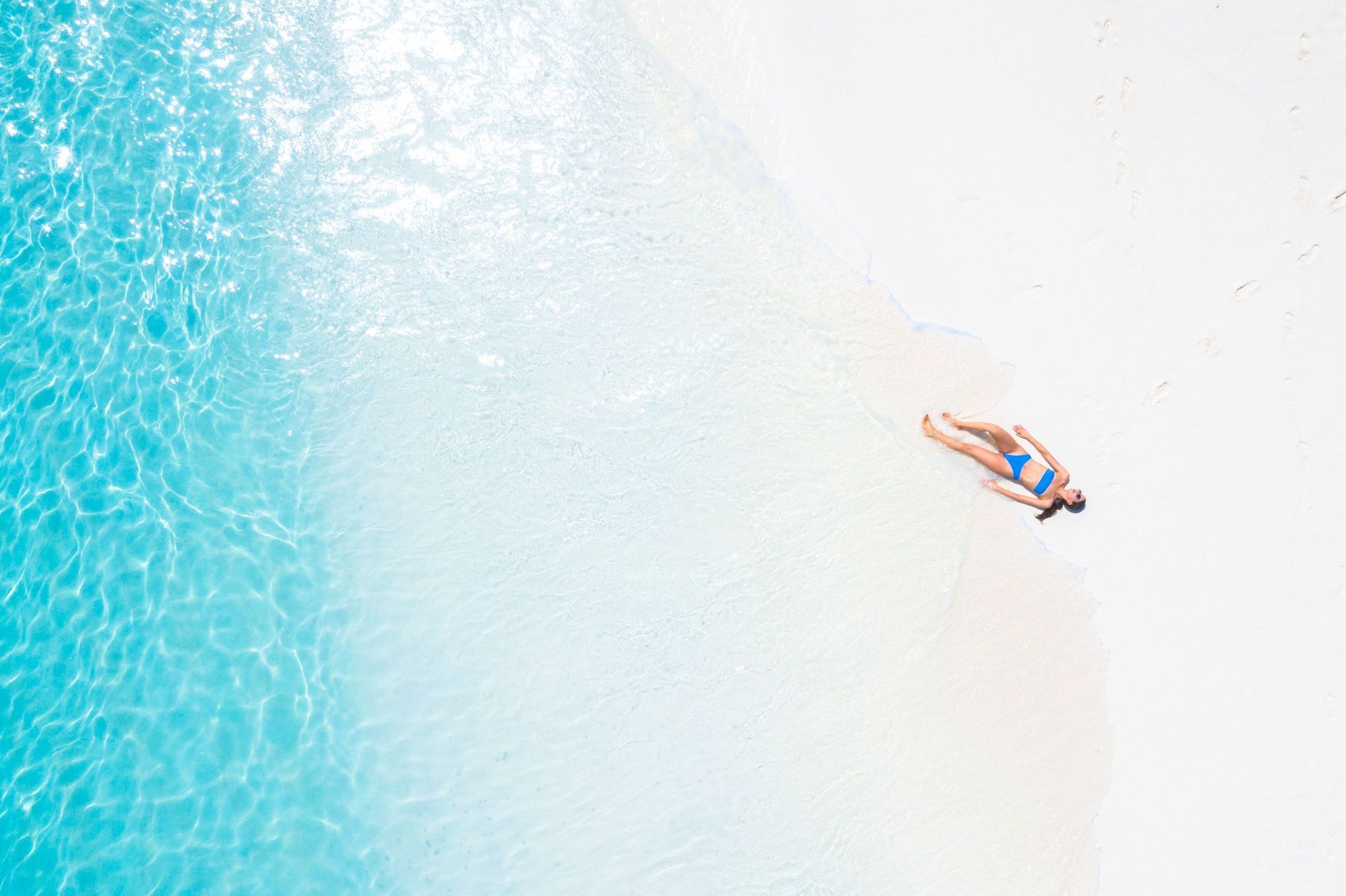 Lone swimmer floating in turquoise water near a bright white shoreline