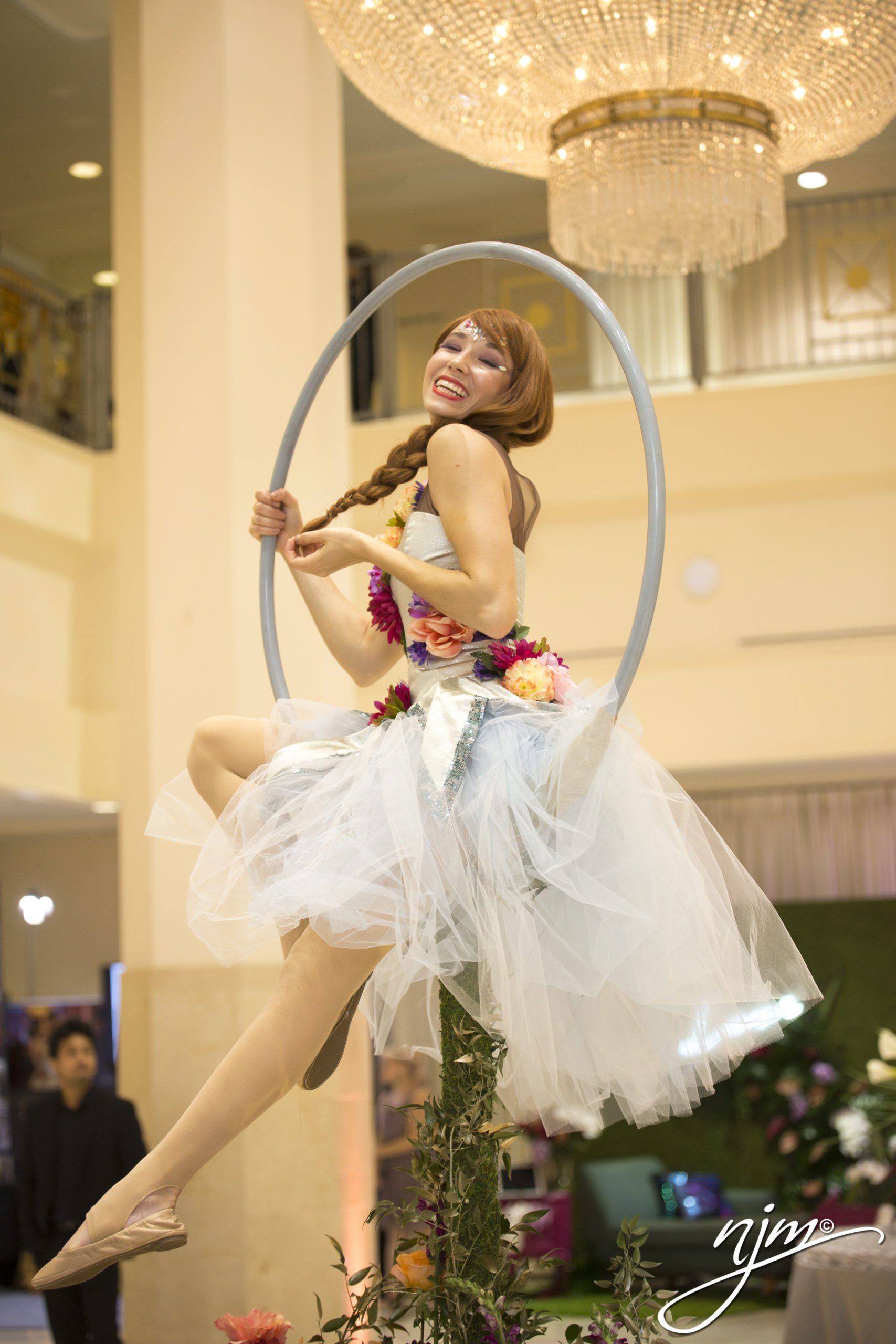 Woman performing aerial hoop dance in a white tutu at an indoor event hall