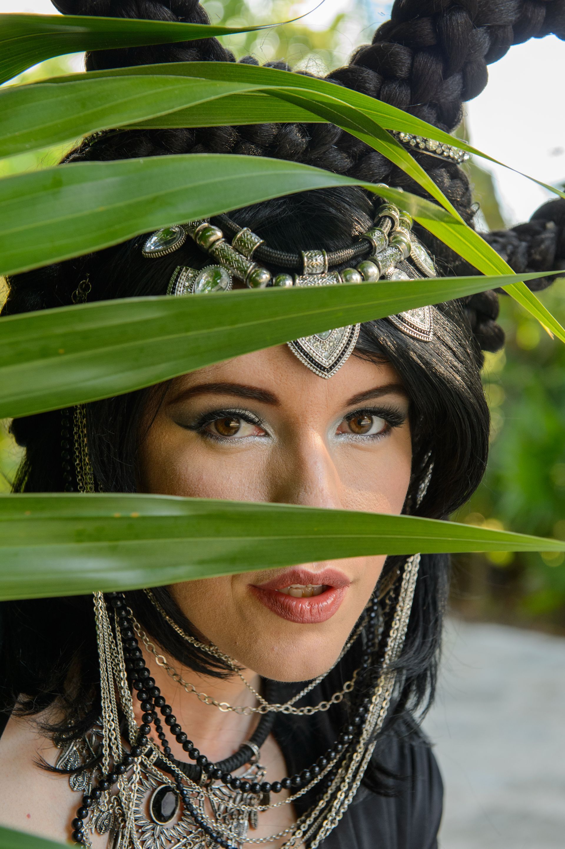 A woman in a costume is hiding behind a palm tree leaf.