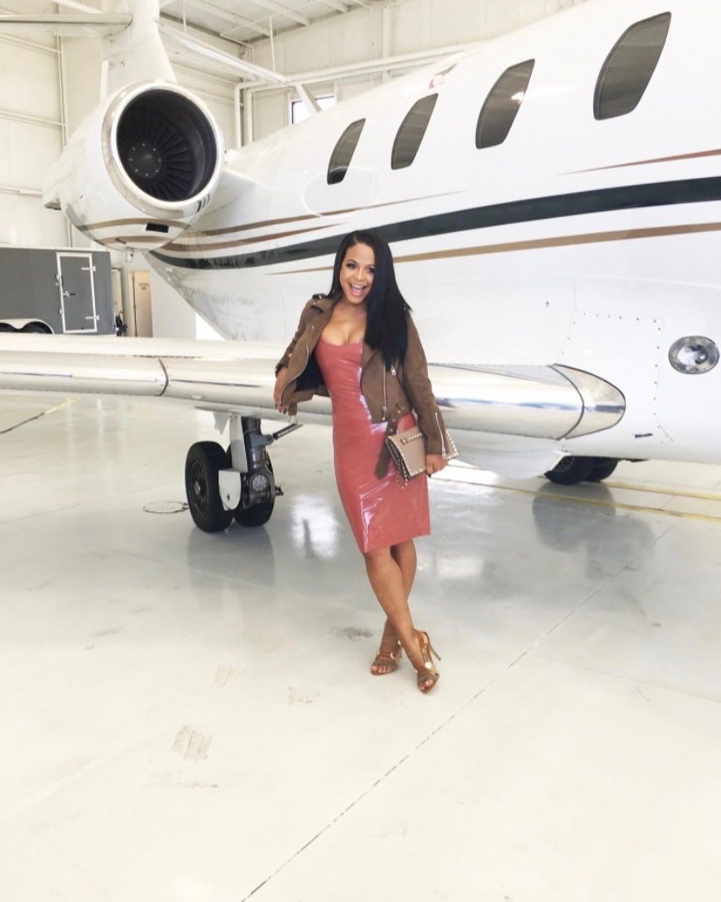 A woman in a red dress is standing in front of a private jet.