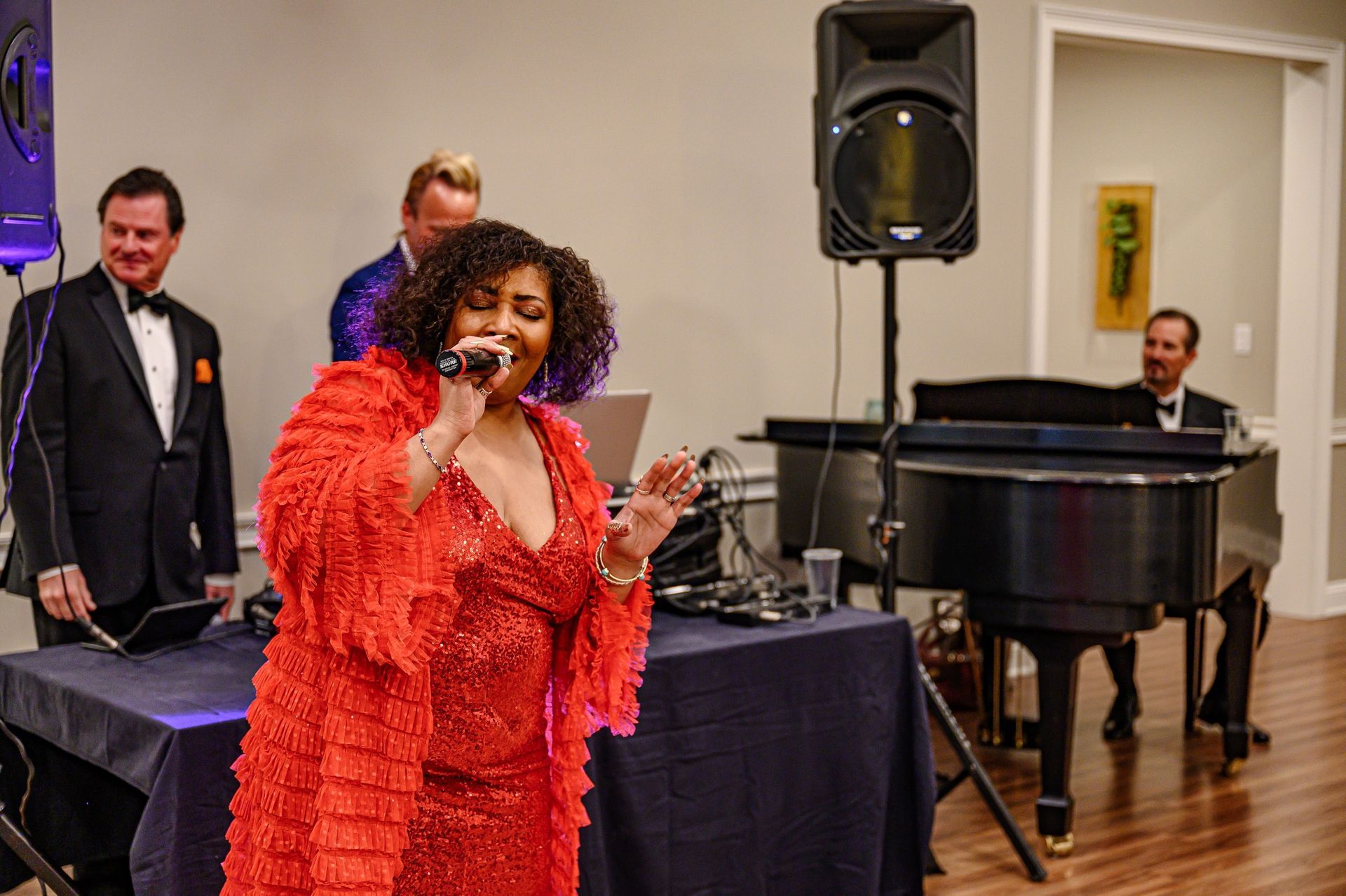 A woman in a red dress is singing into a microphone in front of a piano.