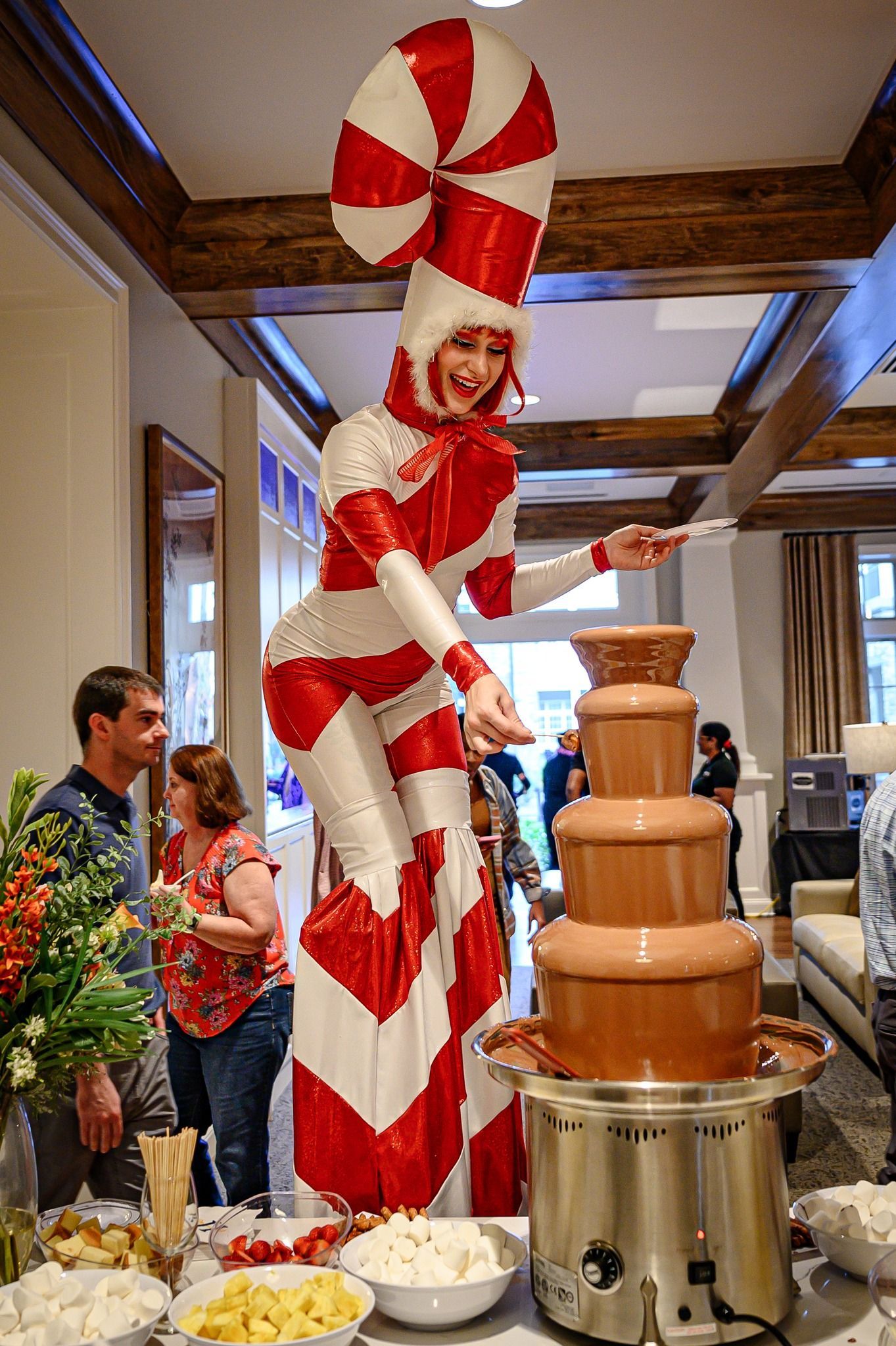 A woman in a candy cane costume is standing on stilts in front of a chocolate fountain.