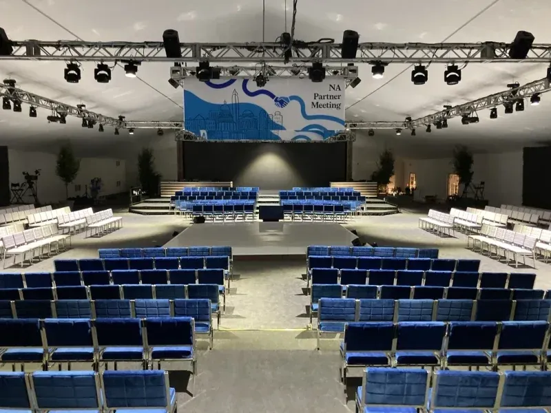 A large auditorium with rows of blue chairs and a stage