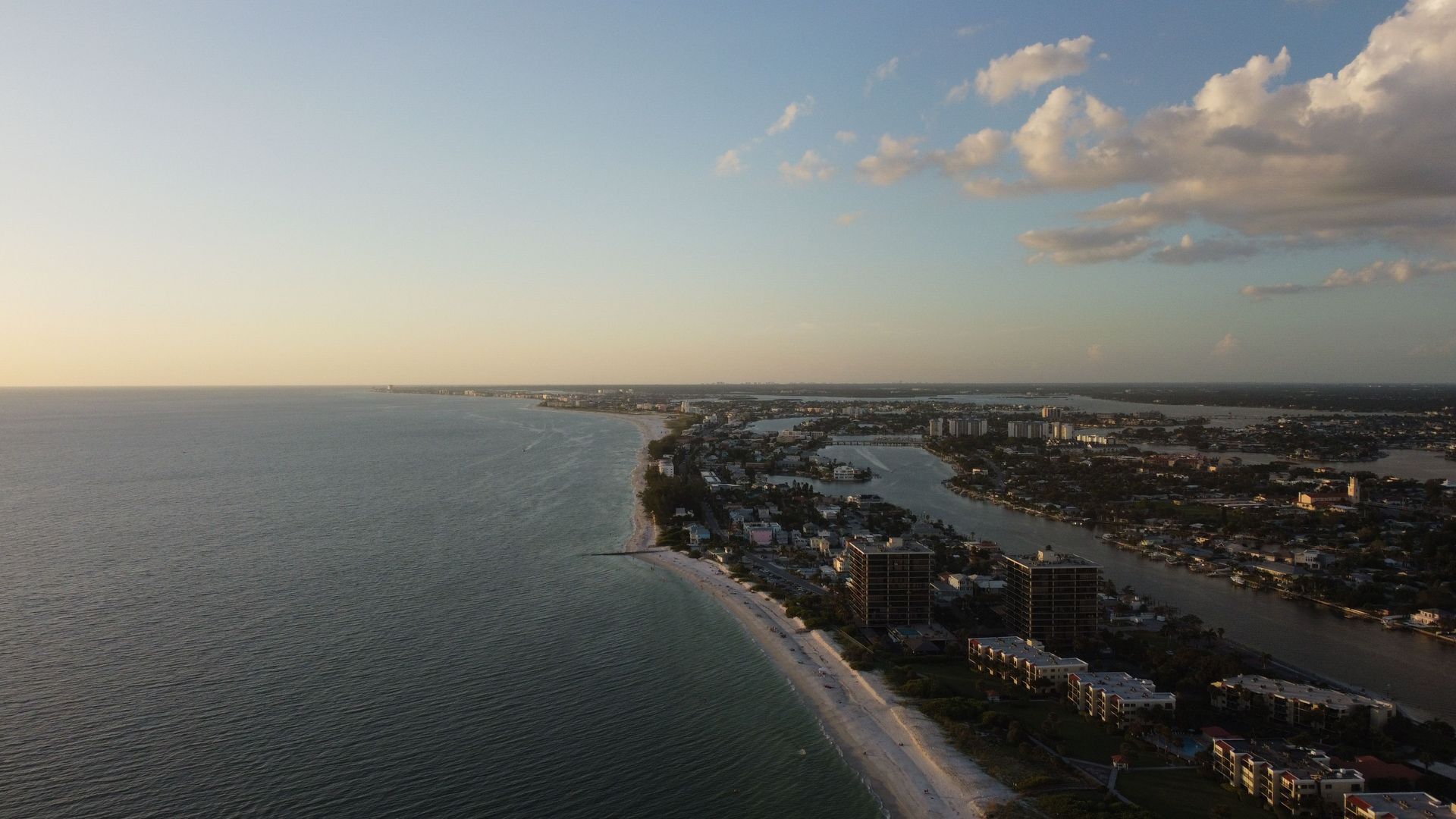 Aerial view of a coastal town with a beach, ocean, and sunset sky