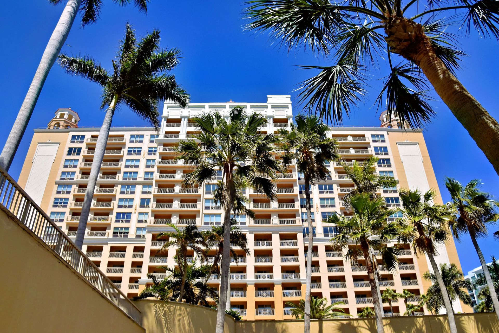 Tall beige apartment building framed by palm trees against a bright blue sky