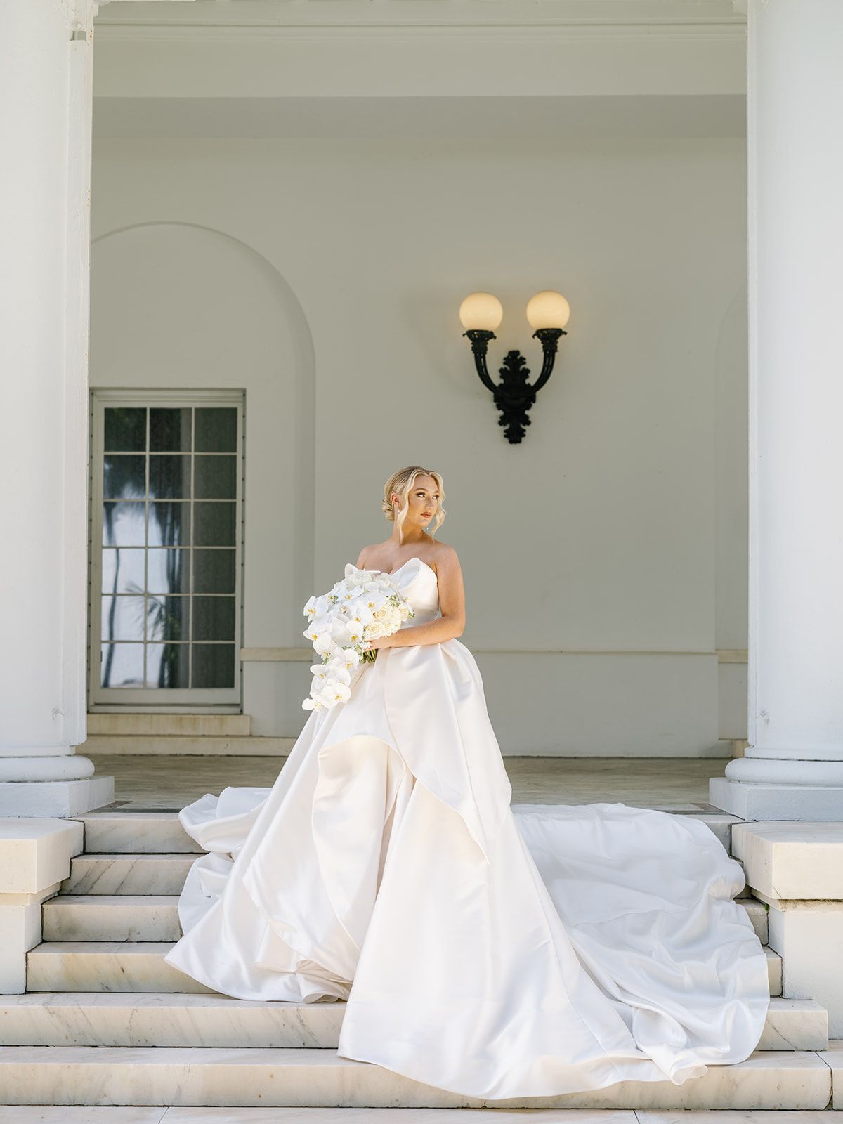 A bride in a wedding dress is standing on a set of stairs holding a bouquet of flowers.