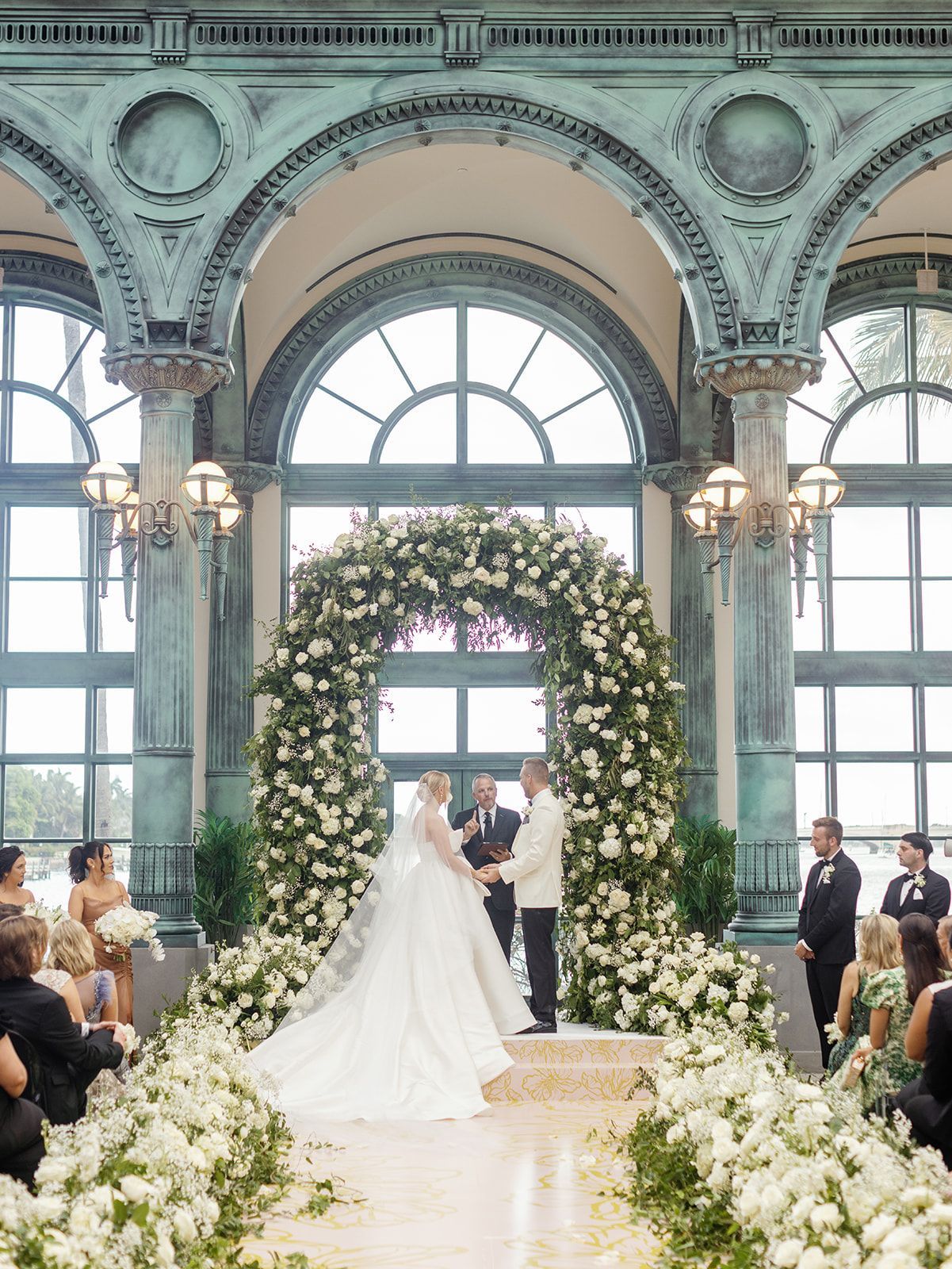 A bride and groom are holding hands during their wedding ceremony in front of a floral arch.