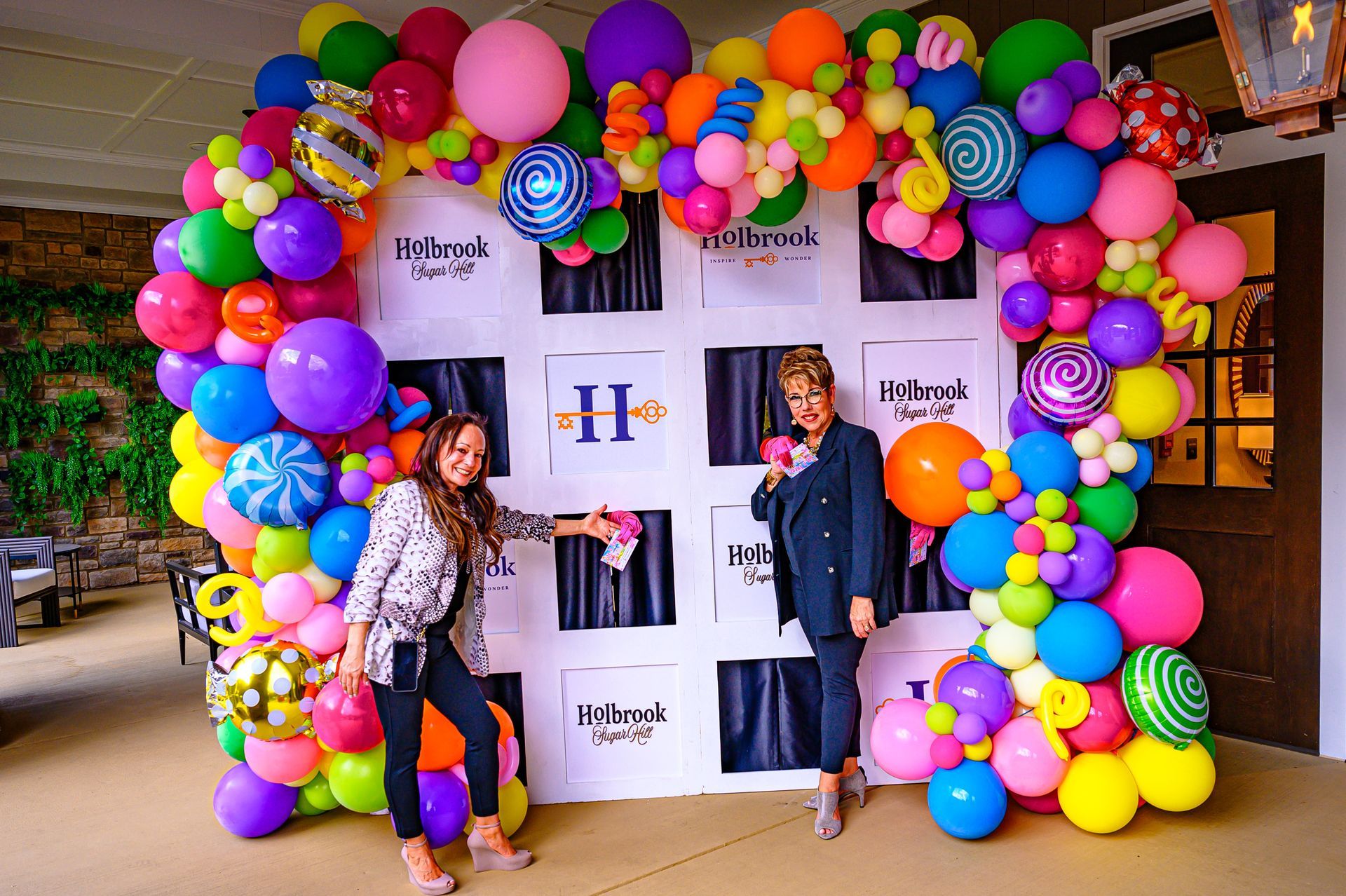 Two women are standing in front of a colorful balloon arch.