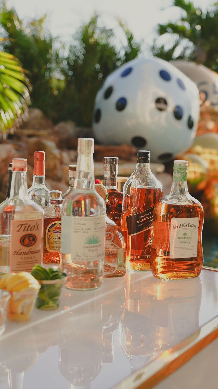 Assorted liquor bottles on a reflective table outdoors, with a giant white golf ball sculpture in the background.