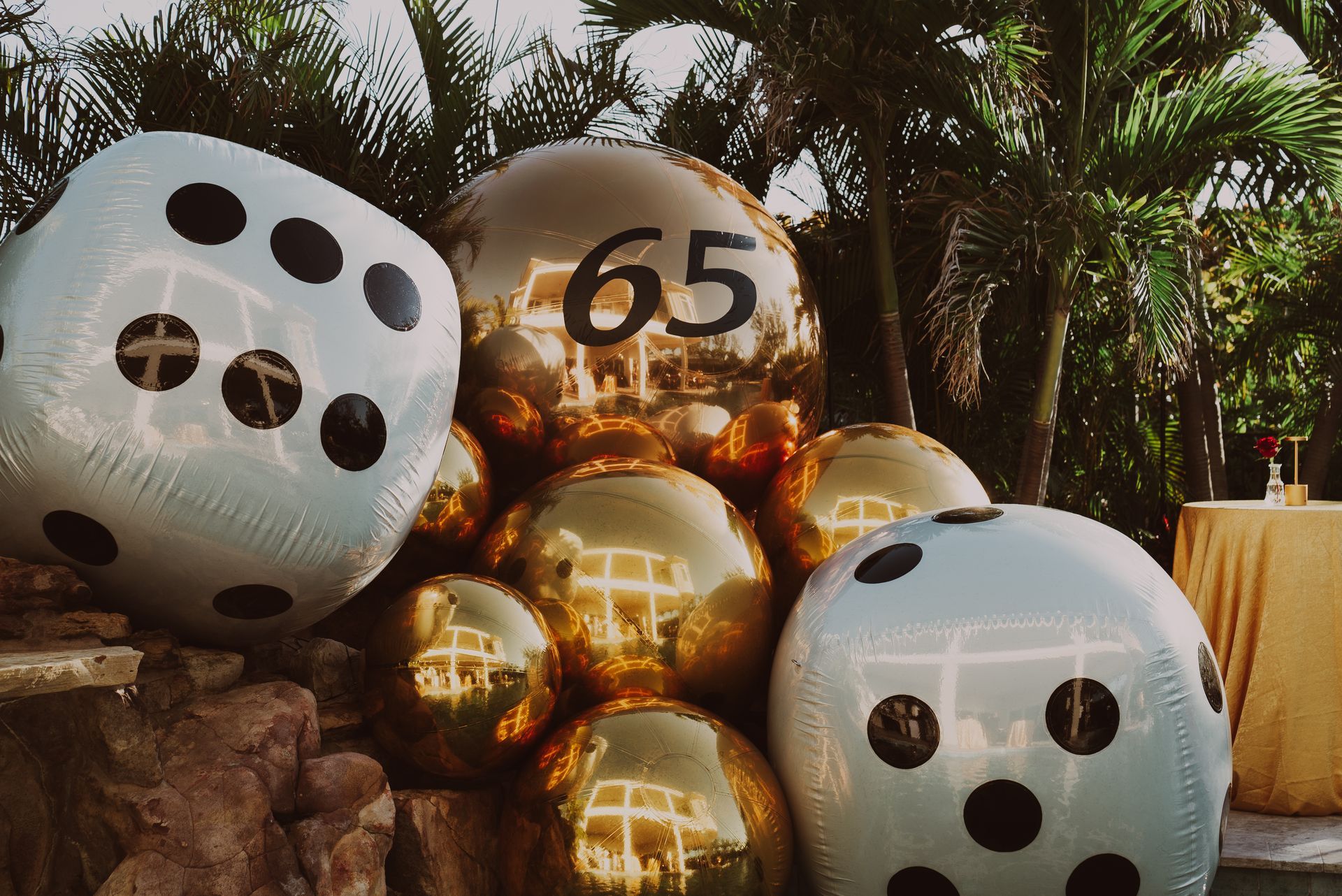 Gold and white reflective balloons with black dots and a “65” at a tropical celebration