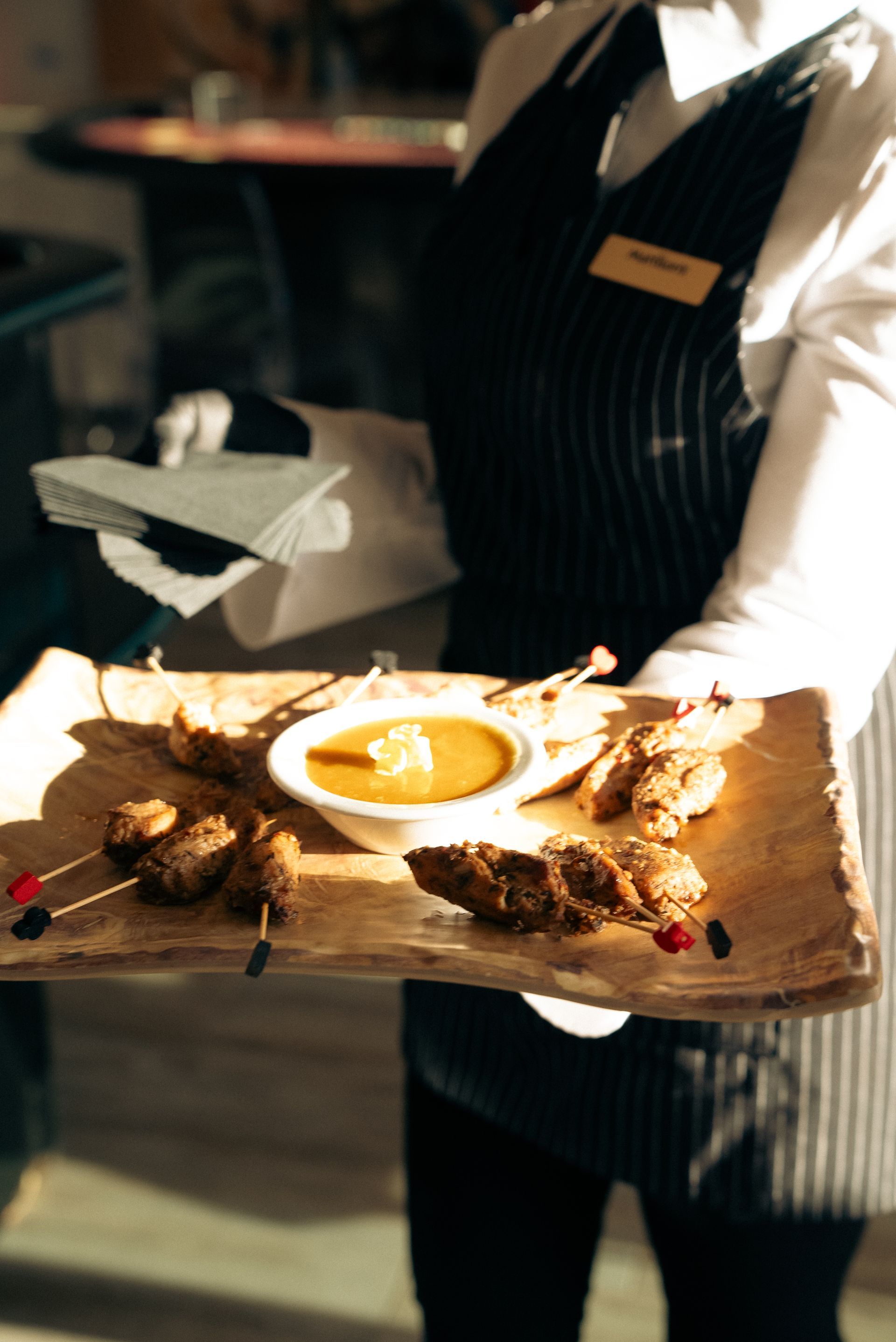 Waiter presenting a plated dish with sauce on a wooden board in a restaurant setting
