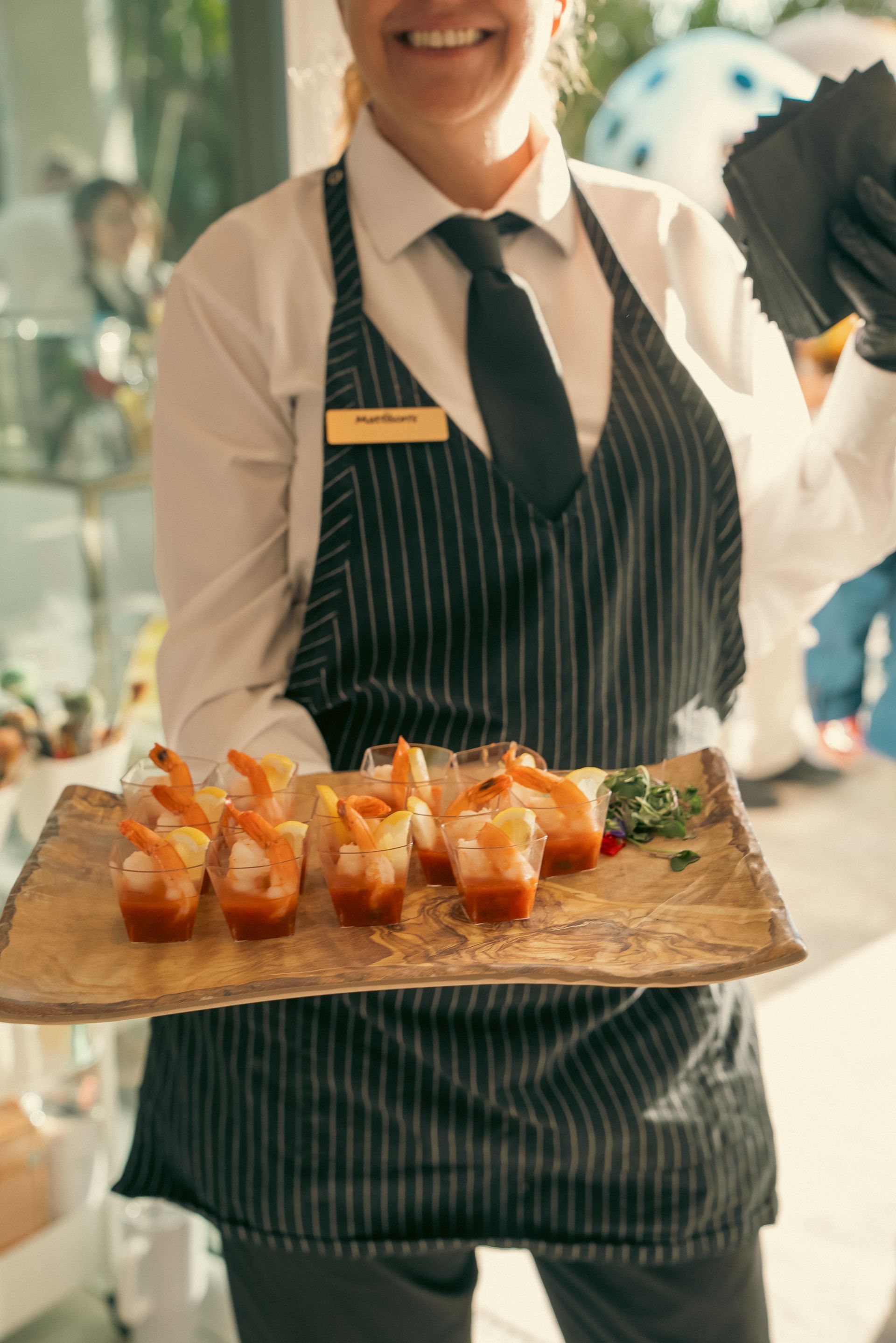 Server in striped apron carrying a tray of orange-topped appetizers at an event