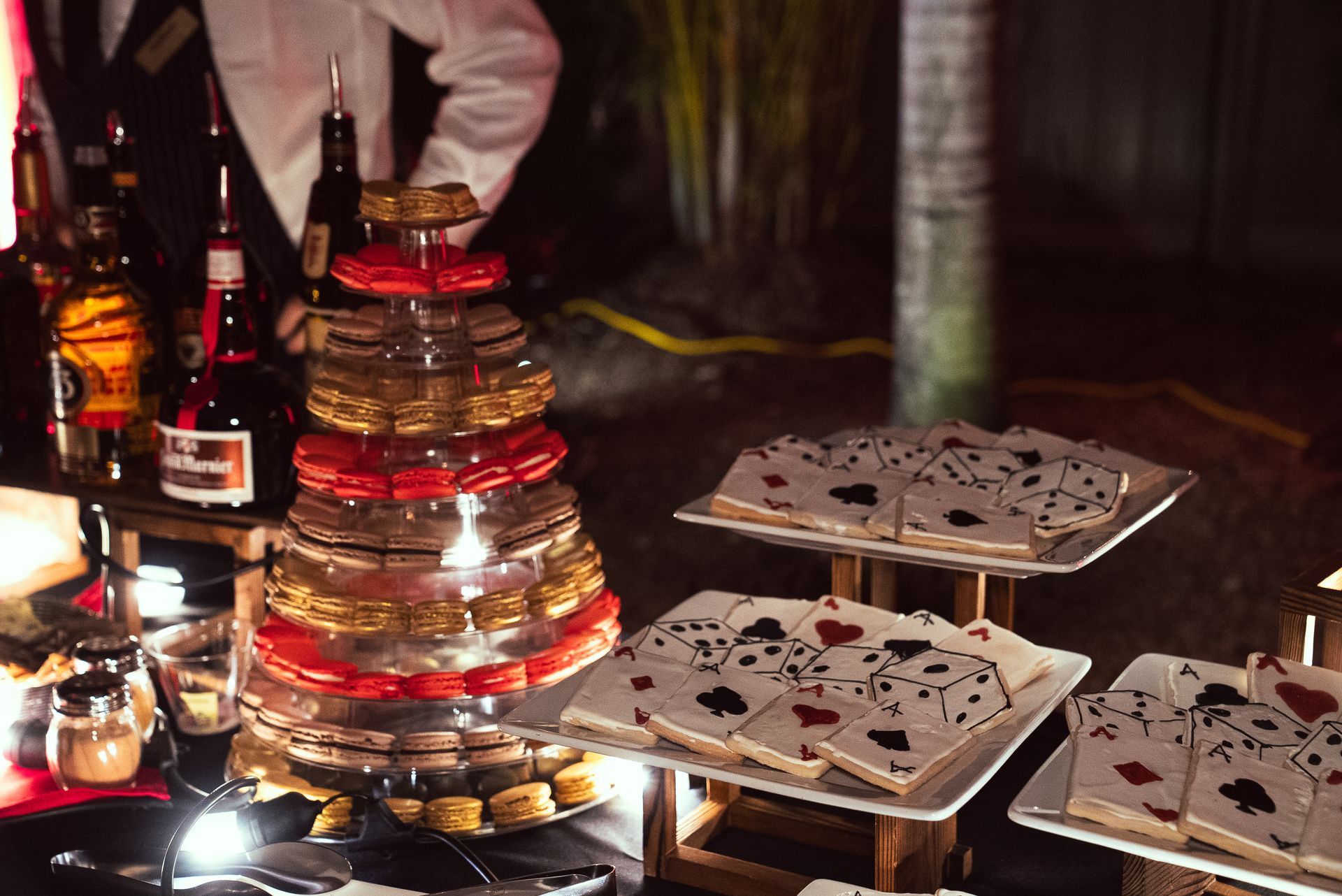 Tiered candle-lit dessert display on a table with white trays and red accents at a dim event.