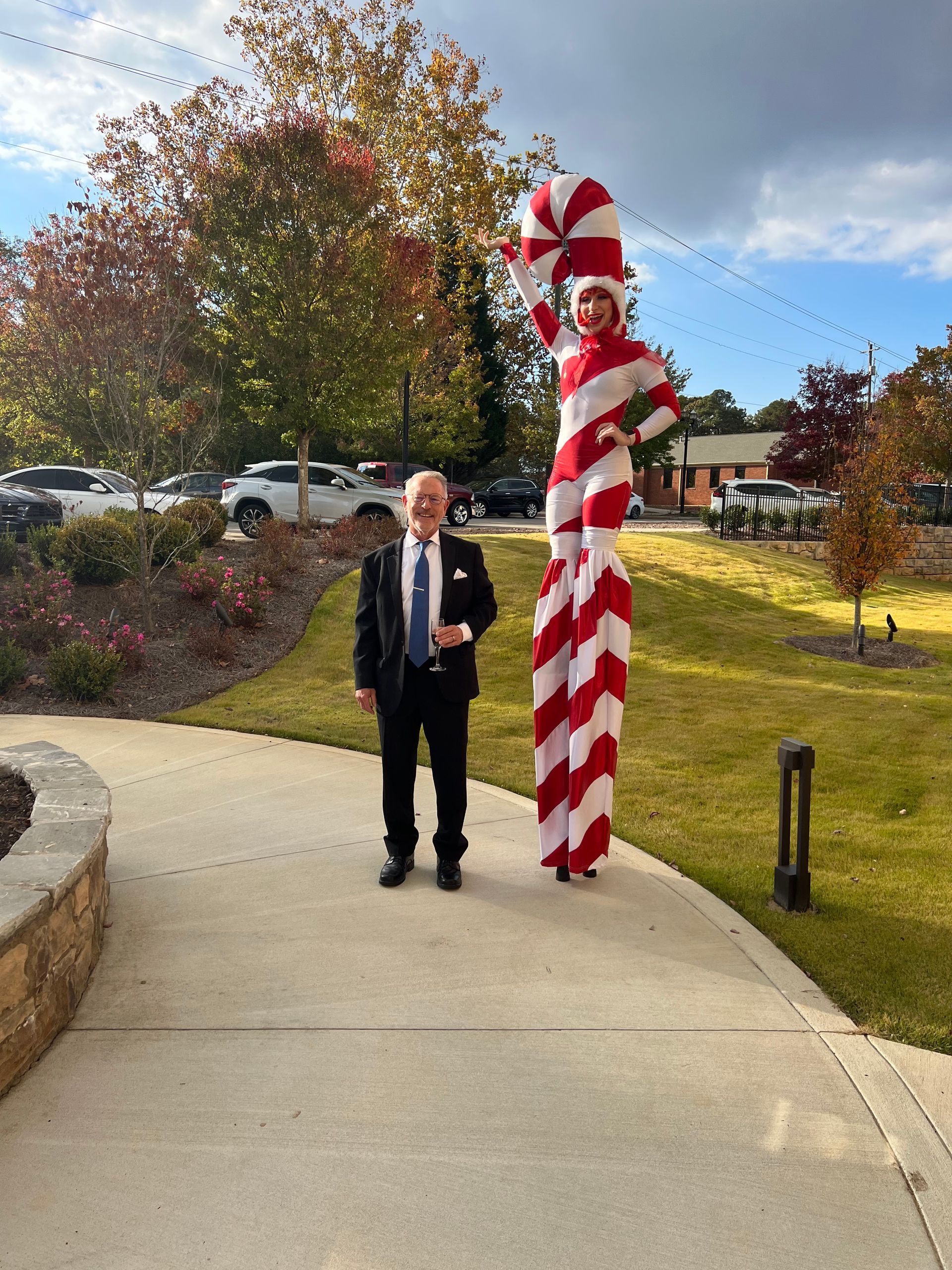 A man in a suit is standing next to a woman on stilts dressed as a candy cane.