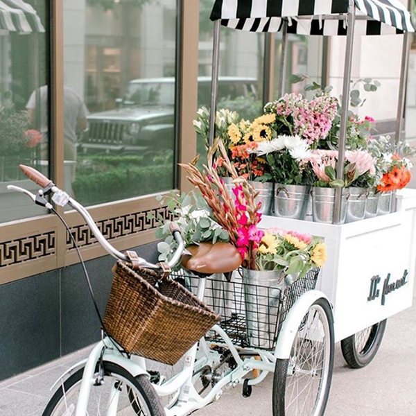 A bicycle is parked next to a cart filled with flowers.