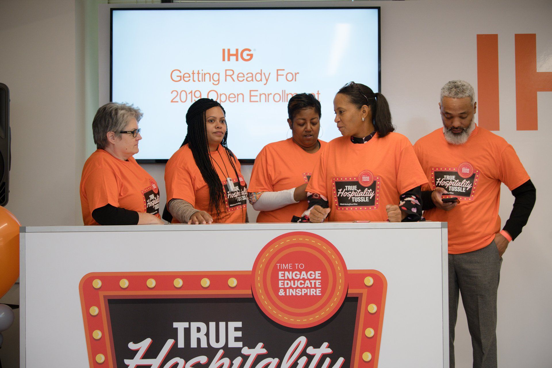 A group of people wearing orange shirts are standing around a table.