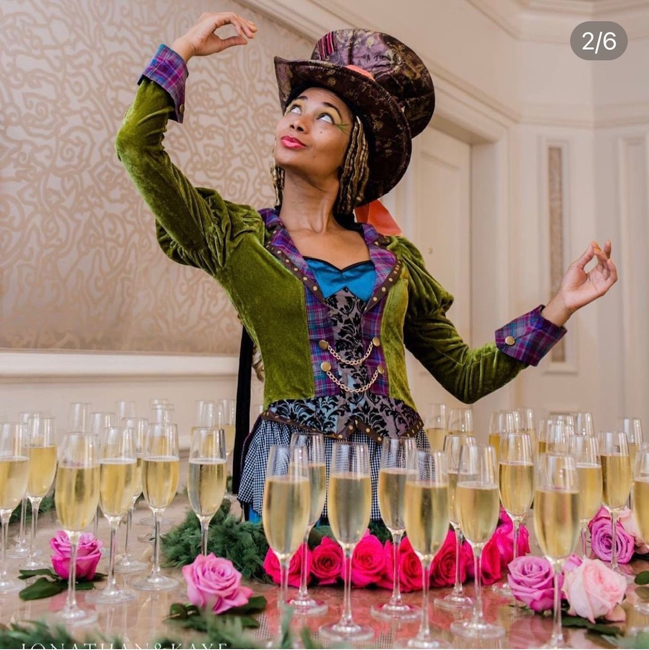 Woman in a velvet costume posing beside champagne flutes and pink roses at a decorated event table