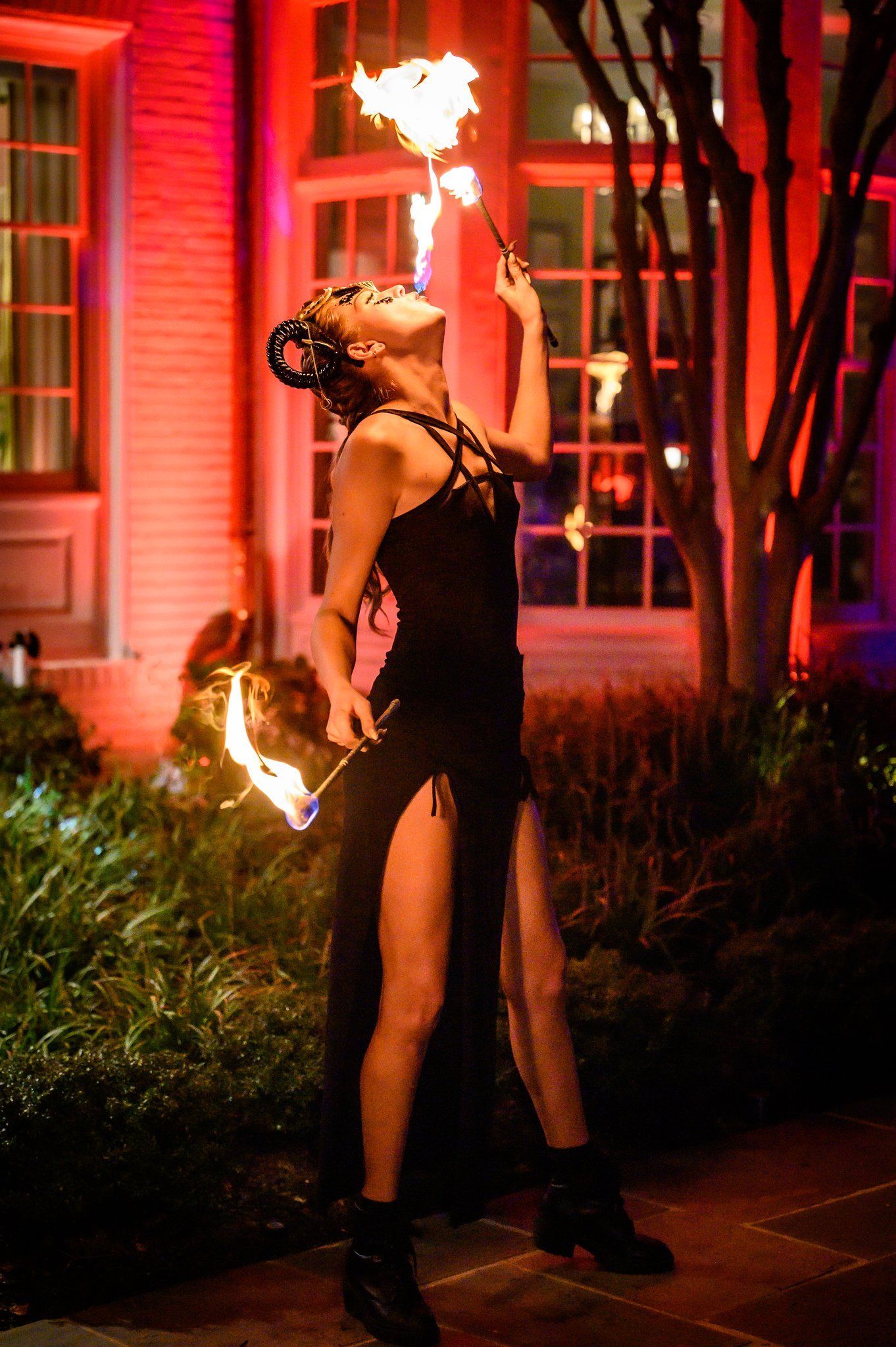 Fire dancer performing with flaming torches at night outside a lit building