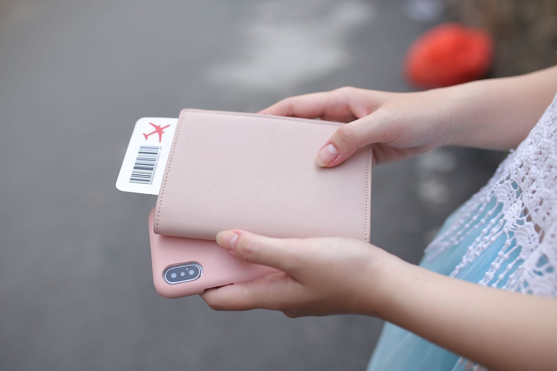 Hands holding a pink wallet with a card sticking out outdoors