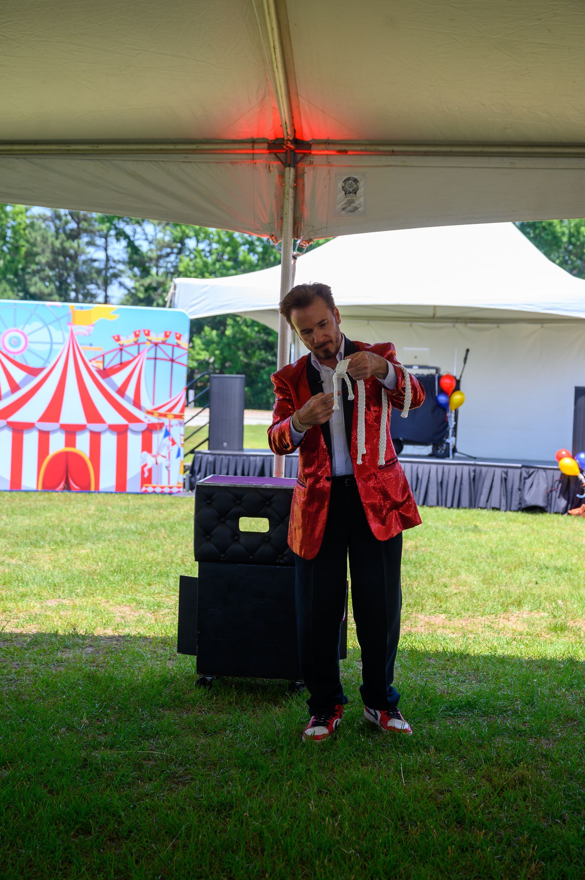 A man in a red jacket is performing a trick in front of a tent.