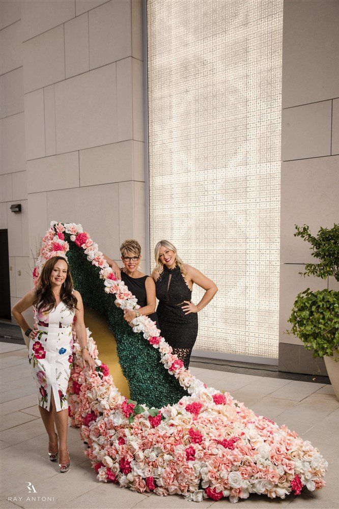 Two women are standing next to a giant shoe made of flowers.
